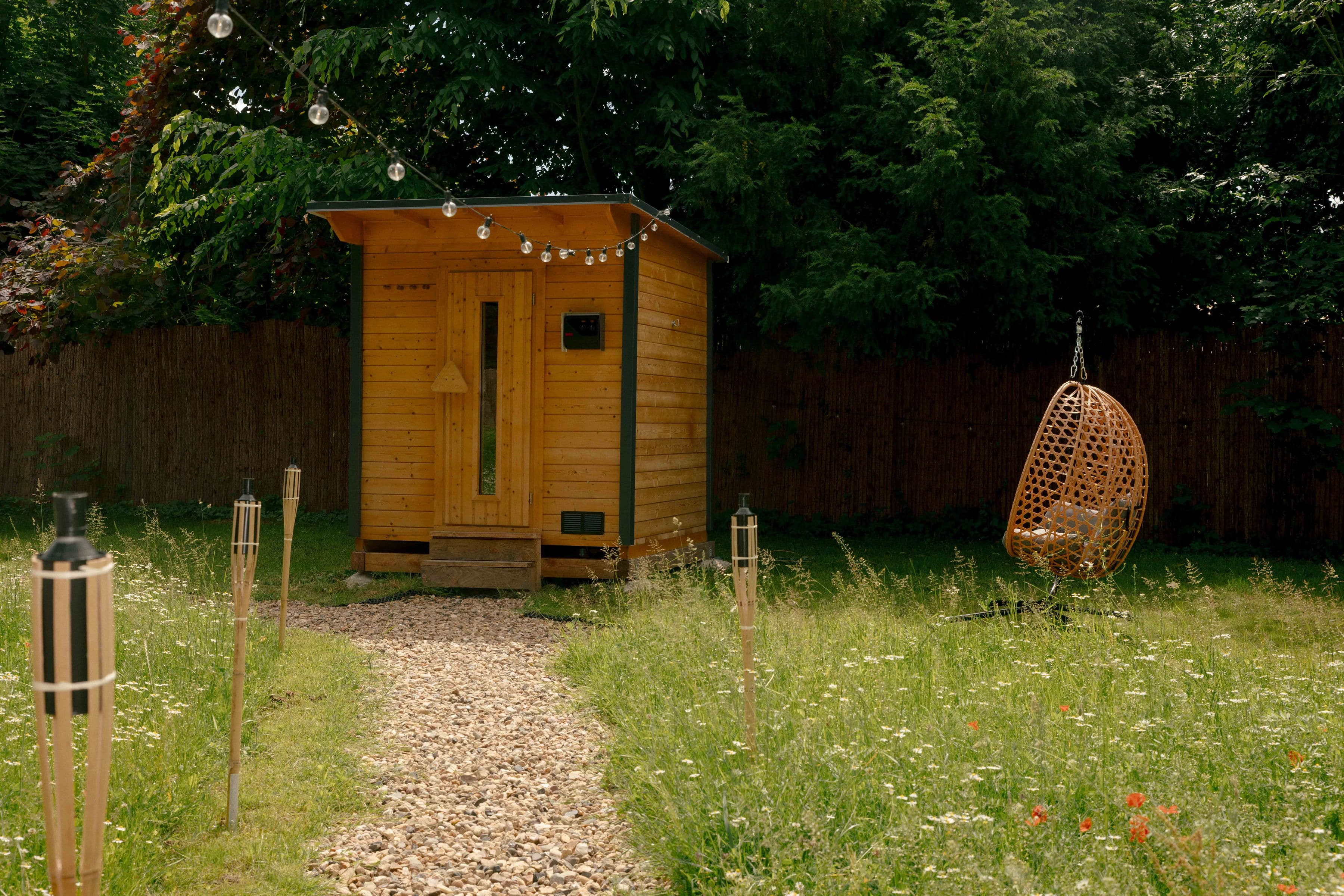 Sauna-Häuschen aus Holz im Garten mit Lichterkette und Hängesessel – privater Wellnessbereich zum Bubble Zelt.